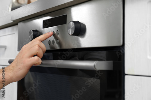 Young man adjusting oven settings in kitchen, closeup