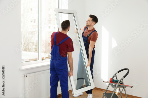 Construction workers installing plastic window in house