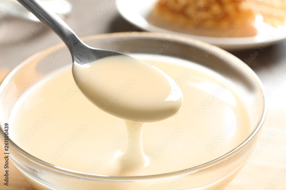 Spoon of pouring condensed milk over bowl on table, closeup. Dairy products Spoon of pouring condensed milk over bowl on table, closeup. Dairy products