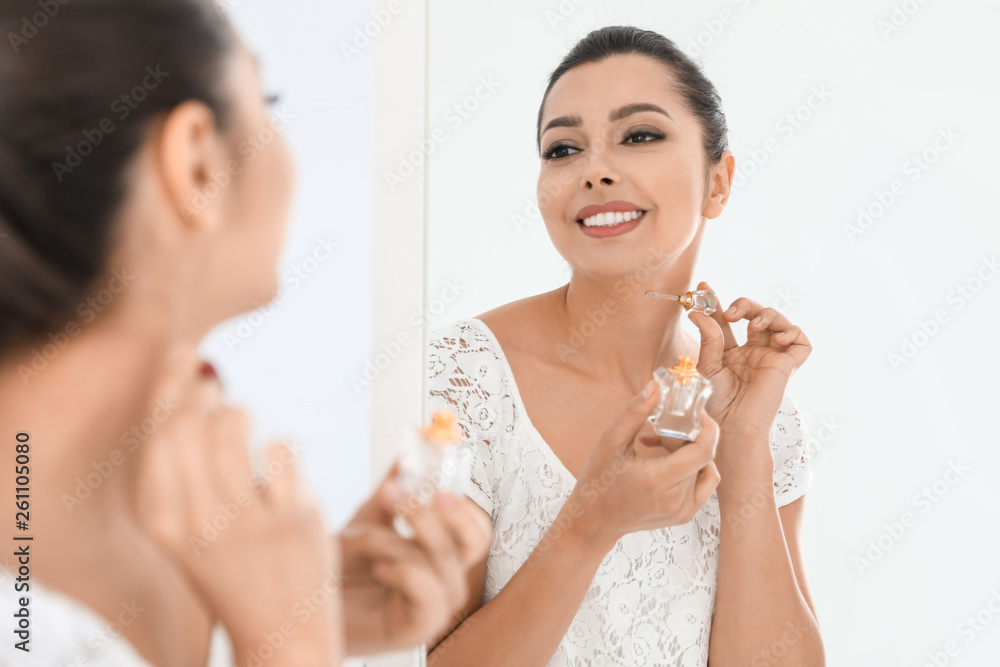 Young woman with bottle of perfume near mirror indoors Young woman with bottle of perfume near mirror indoors