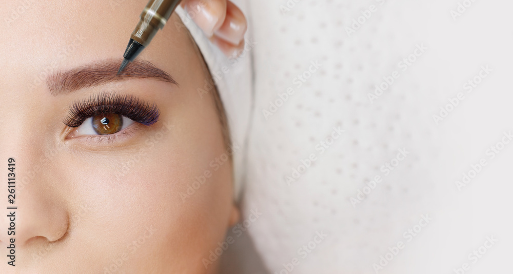 Beautiful young girl with long eyelashes tweezing her eyebrows in a beauty salon. Woman doing eyebrow permanent makeup correction . Microblading brow. - obrazy, fototapety, plakaty 