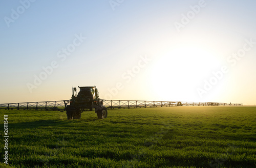 Tractor on the sunset background. Tractor with high wheels is making fertilizer on young wheat. The use of finely dispersed spray chemicals