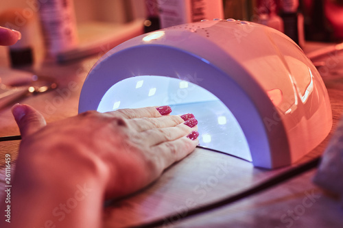 Client at manicure salon dryes gel nails in UV light photo