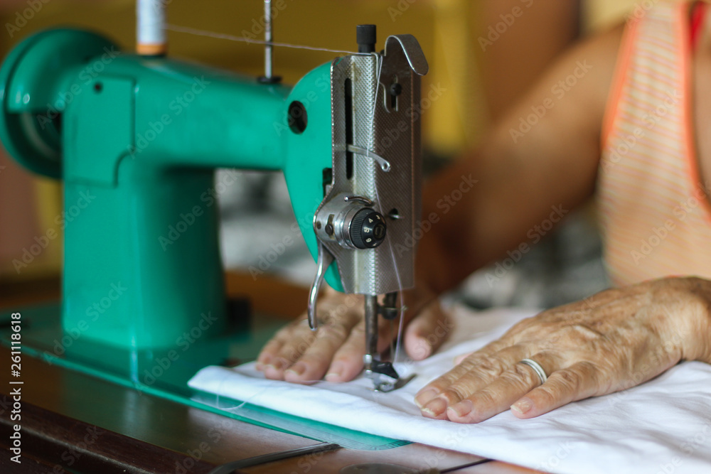 Fototapeta premium Sewing process - Women's hand behind her sewing. Vintage sewing machine isolated - Concept for needlework and tailoring.