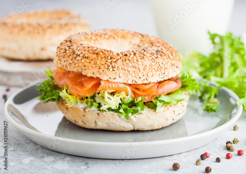 Fresh healthy bagel sandwich with salmon, ricotta and lettuce in grey plate on light kitchen table background. Healthy diet food. Glass of milk and fresh vegetables