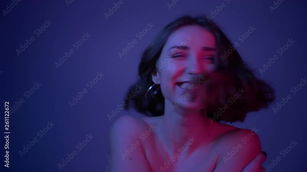 Closeup shoot of young cute female smiling and hugging herself in front of the camera with neon blue background Closeup shoot of young cute female smiling and hugging herself in front of the camera with neon blue background