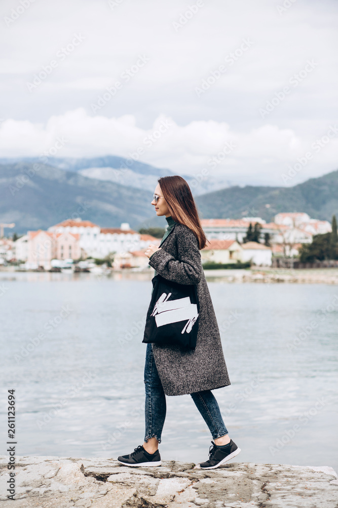 Beautiful young trendy girl walks near the sea against the backdrop of Tivat in Montenegro.