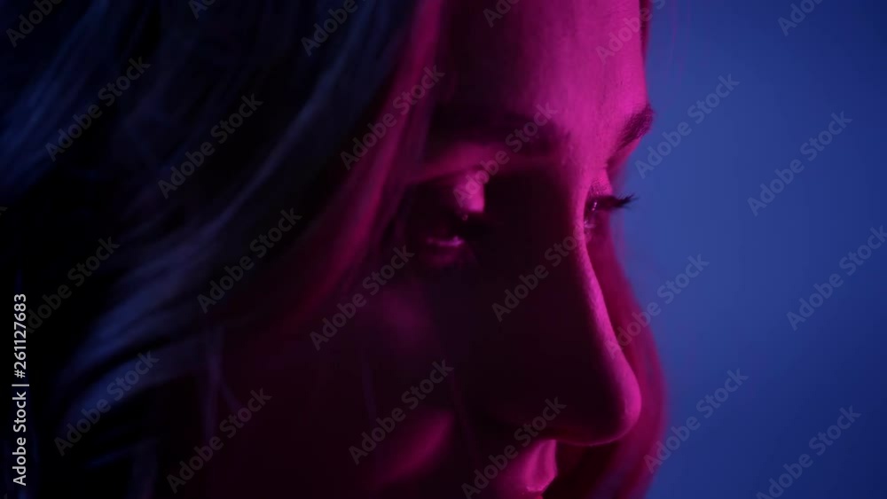 Closeup side view shoot of young pretty female face smiling happily in front of the camera with neon blue background Closeup side view shoot of young pretty female face smiling happily in front of the camera with neon blue background