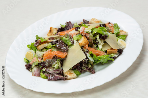 salad with greens, quail eggs and salmon, on a white oval plate