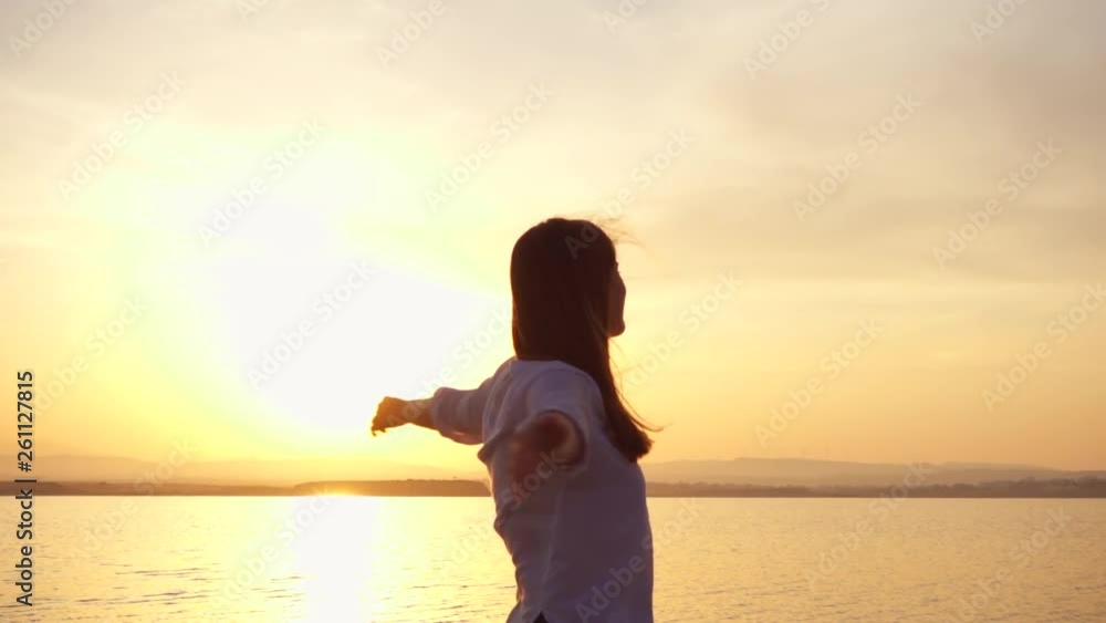 Dark silhouette of young woman raising arms up and dancing at sunset on lake. Female figure outstretching hands at golden hour in slow motion Dark silhouette of young woman raising arms up and dancing at sunset on lake. Female figure outstretching hands at golden hour in slow motion