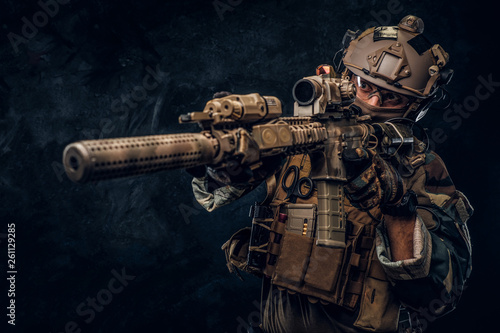 Obraz na płótnie Elite unit, special forces soldier in camouflage uniform holding an assault rifle with a laser sight and aims at the target