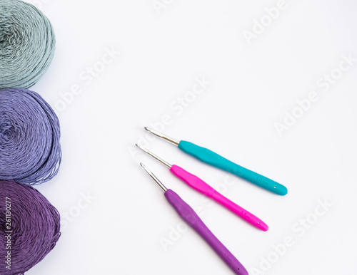 Multi-colored balls of wool for crocheting and needlework and crochet hooks on a white background