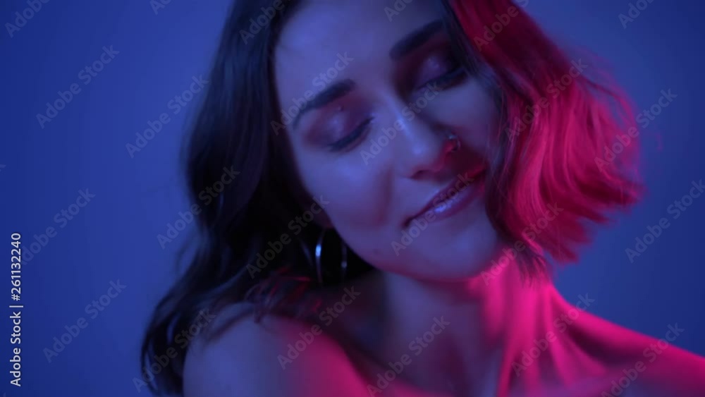 Closeup side view shoot of young cheerful female face smiling happily turning to camera with neon blue background Closeup side view shoot of young cheerful female face smiling happily turning to camera with neon blue background