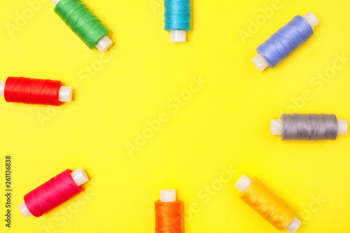 Handicraft background. Set of multicolored spools of thread form frame on yellow background with copy space. Accessories for needlework, embroidery, sewing. Flat lay. Top view.