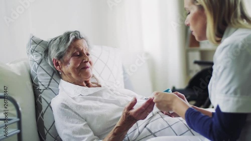 Health visitor giving pills to a sick senior woman lying in bed at home. photo