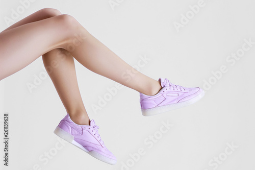 Stylish female shoes in pastel colors. Flat lay. Beautiful woman legs in purple sneakers on gray background. Beauty, fashion, minimal idea creative concept.
