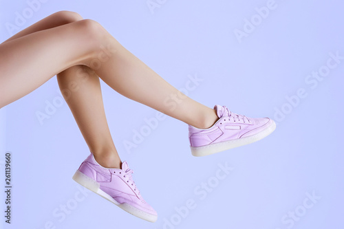 Stylish female shoes in pastel colors. Flat lay. Beautiful woman legs in purple sneakers on blue background. Beauty, fashion, minimal idea creative concept.