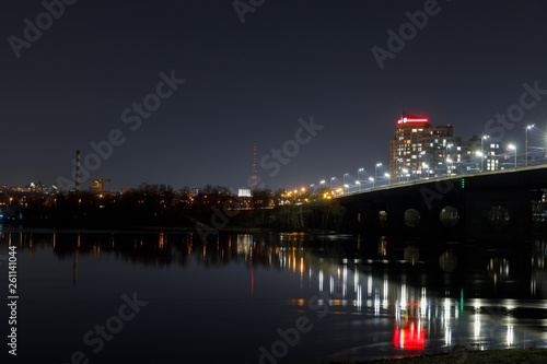 dark cityscape with illuminated buildings, bridge and river