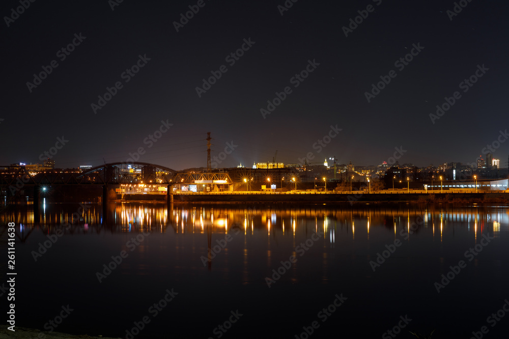 dark cityscape with river and illuminated buildings on shore at night