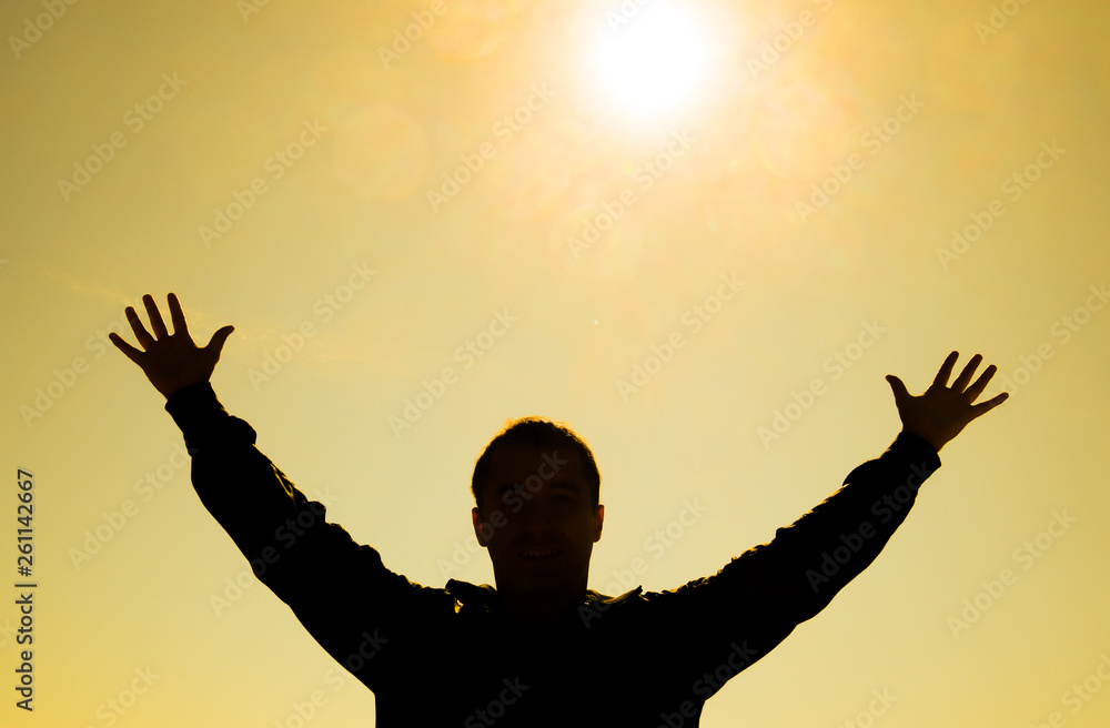 Silhouette of a man against the background of the sun and yellow at sunset sky. Hands are raised up to the sun Silhouette of a man against the background of the sun and yellow at sunset sky. Hands are raised up to the sun