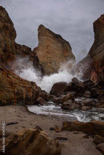 wave crashing through rocks on a dark, dramatic, moody day