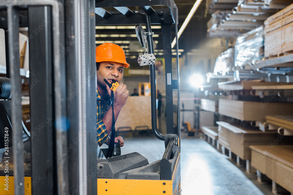 handsome indian worker sitting in forklift machine in warehouse and talking  on walkie talkie Stock Photo | Adobe Stock
