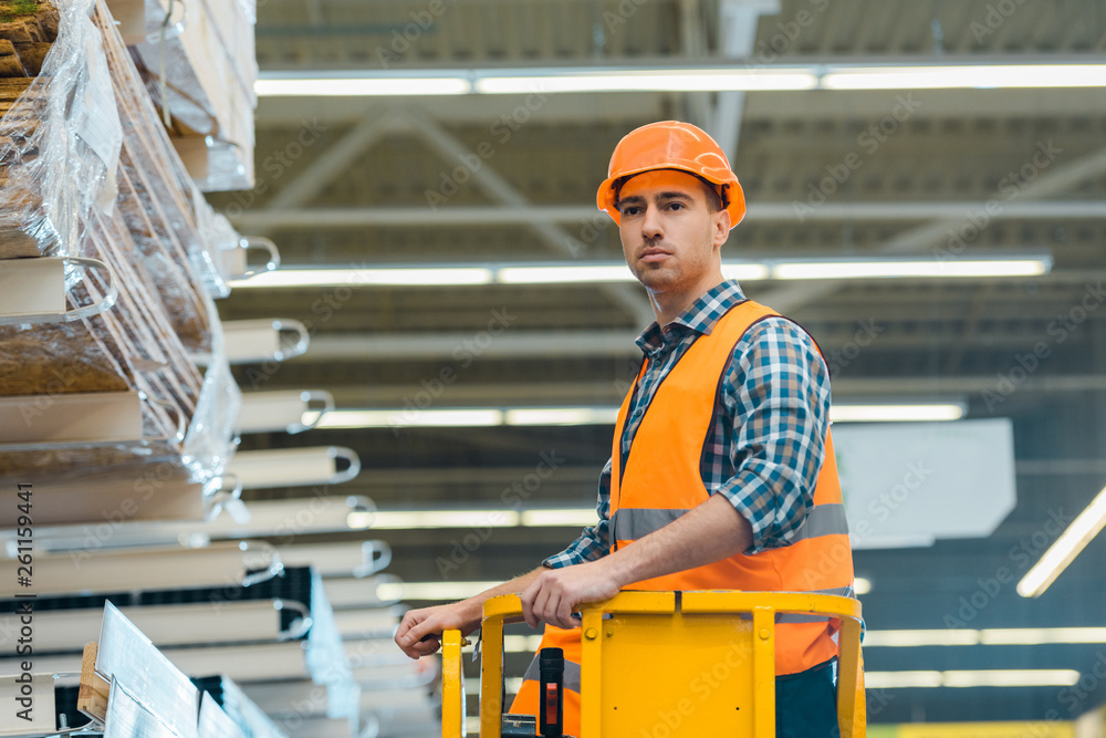 handsome, serious worker standing on scissor lift in warehouse handsome, serious worker standing on scissor lift in warehouse