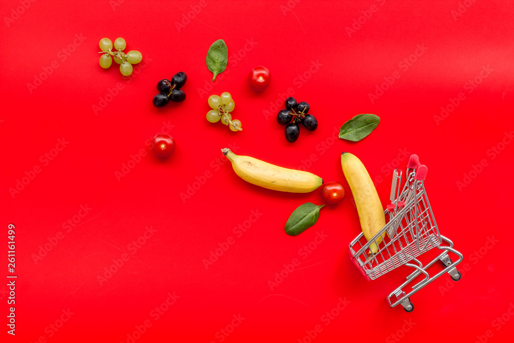 buying products with fruits and mini trolley on red background top view space for text