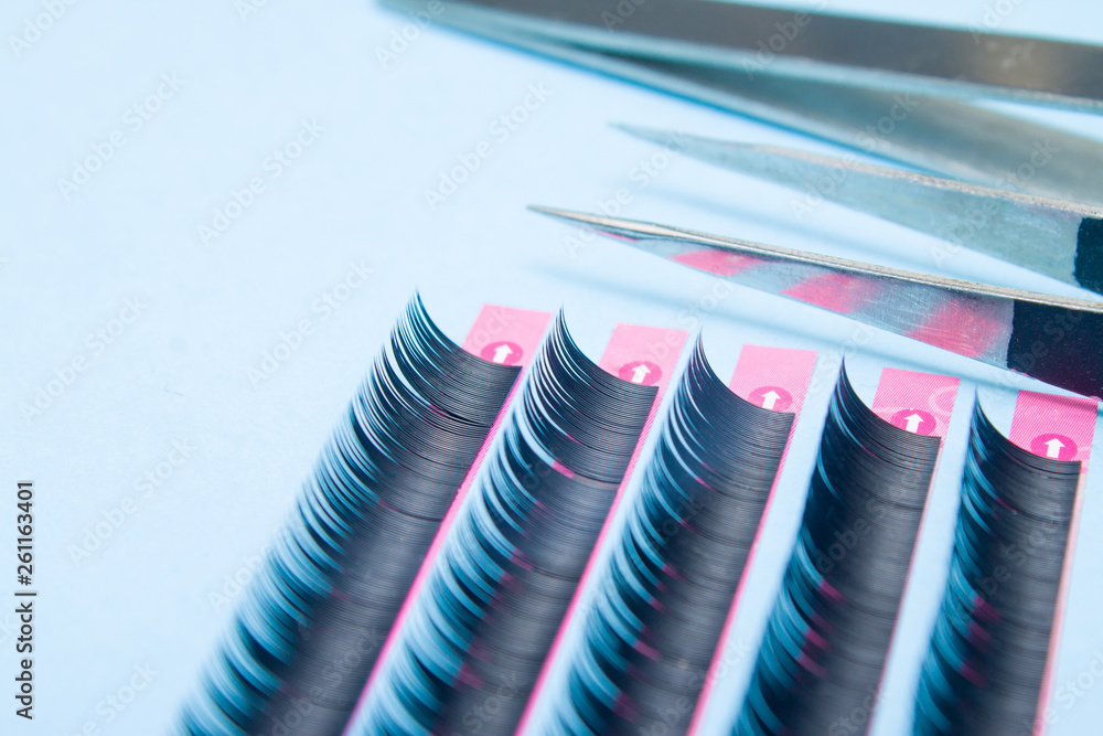 tools for Eyelash Extension Procedure. Two tweezers with artificial black lashes on blue background. copyspace mockup - Beauty and fashion concept