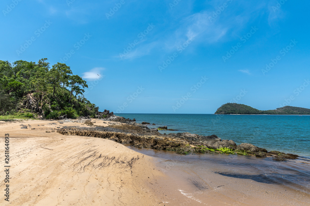 Cairns, Australia - February 18, 2019: North end of warm beige tropical beach and rocks of Palm Cove with azure Coral Sea water under blue sky. Double Island in back.