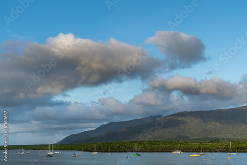 Cairns, Australia - February 18, 2019: Evening shot at sunset. Anchored small sailing boats on Chinaman Creek under heavy cloudscape. Backdrop is rainforest hills.