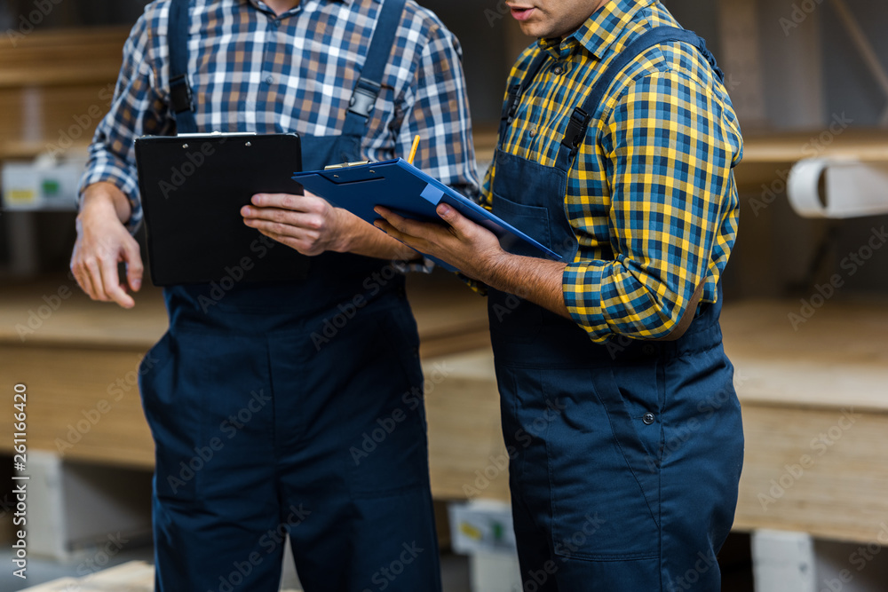 cropped view of two multicultural warehouse workers in uniform holding clipboards