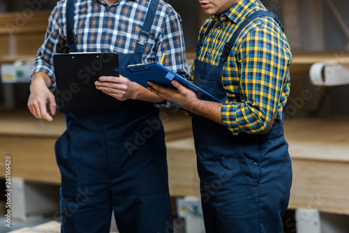 cropped view of two multicultural warehouse workers in uniform holding clipboards