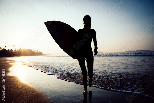 Surfer  woman walking with surfboard on the beach at sunrise © lzf