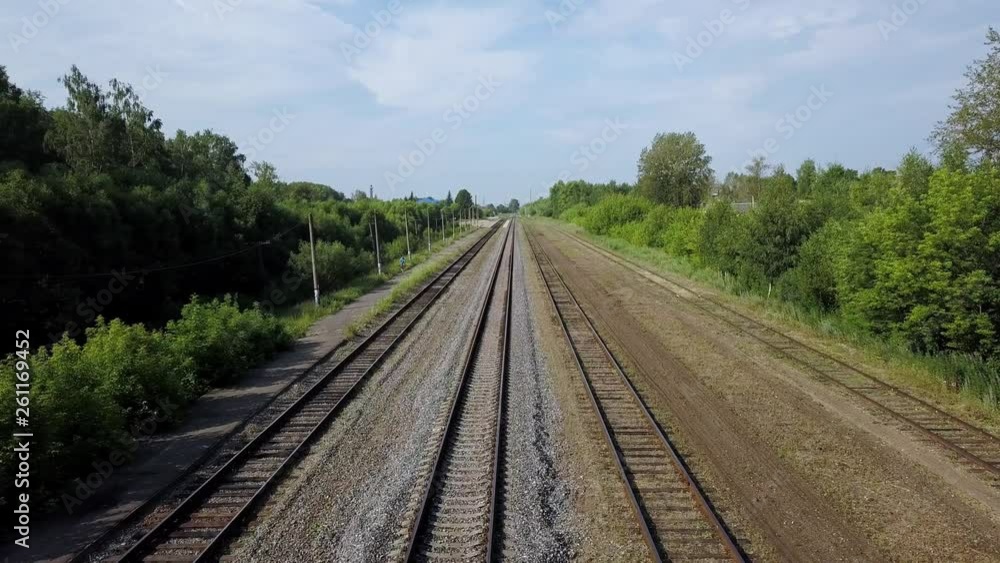 Four rows of long empty railways are laying between green line of wild bushes and high trees at some suburb area on warm summer sunny day. Four rows of long empty railways are laying between green line of wild bushes and high trees at some suburb area on warm summer sunny day.