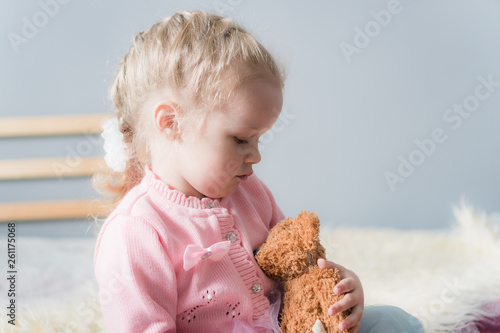 A little girl in a pink sweater is cradling a toy