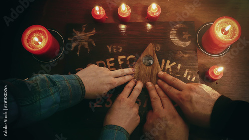Two people conducting a seance using a Ouija Board, or Talking Spirit Board, with red candles. Shot from overhead.