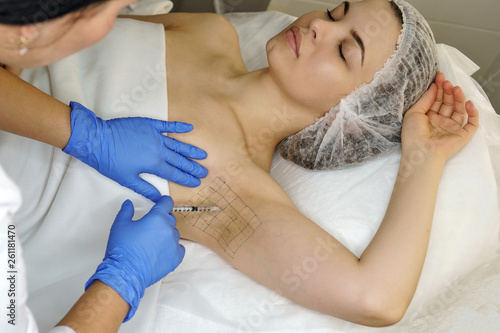 Hands of cosmetologist are close-ups injecting hyaluronic acid into armpit area of girl. Treatment of hyperhidrosis. Cosmetic procedure in spa salon. photo