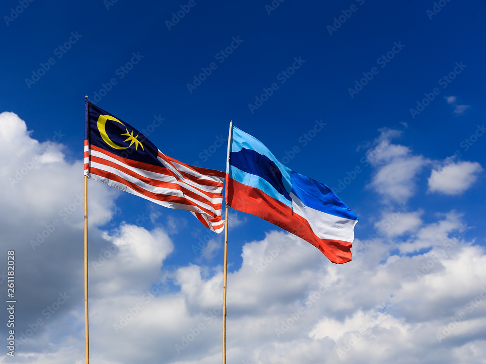 Malaysia and Sabah flags waving against blue sky.