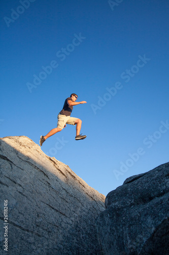 A young man outdoors leaping from one boulder to another in the Sierra Nevada Mountains of Northern California. © Ben