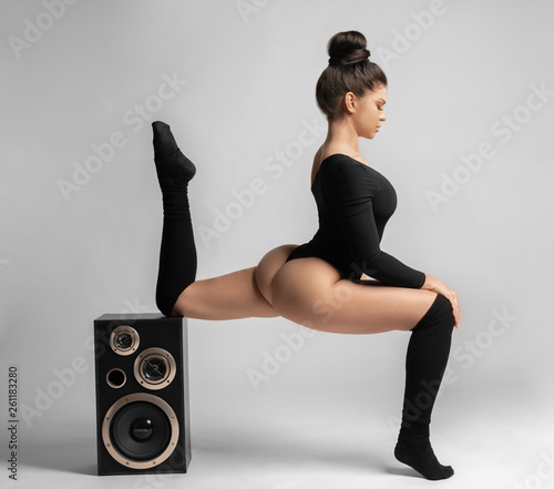 Beautiful brunette woman in black bodysuit sits and leans on a music speaker. photo