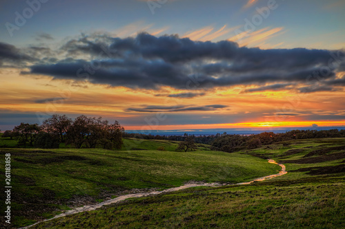A stream passing through a green field with a sunset in the background on Table Mountain in Northern California.