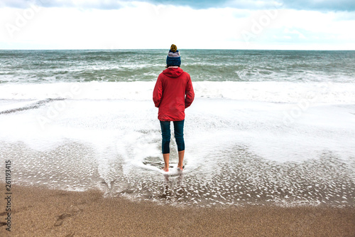 Barefoot woman looks at the winter sea.