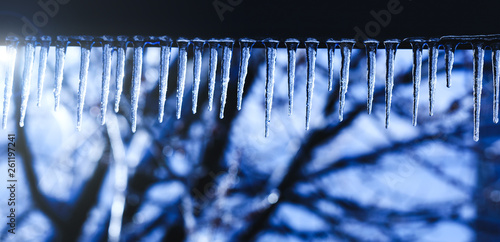 Magic crystal icicles hanging from roof. Melting icicle with falling shiny drops over a beautiful bright background. Ice stalactites in the cold winter or spring in Canada.