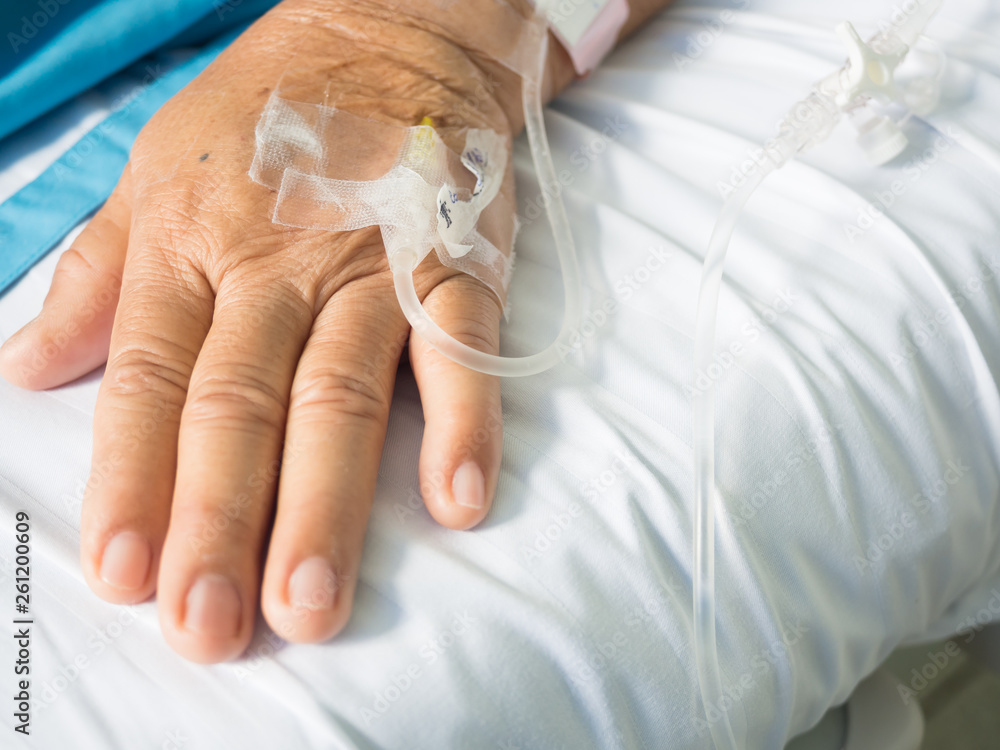 Fototapeta premium Close up old woman patient hand and iv set for fluid intravenous drop saline drip on white hospital bed background in the hospital room.Medical treatment emergency patient.Seriously patient admitted.
