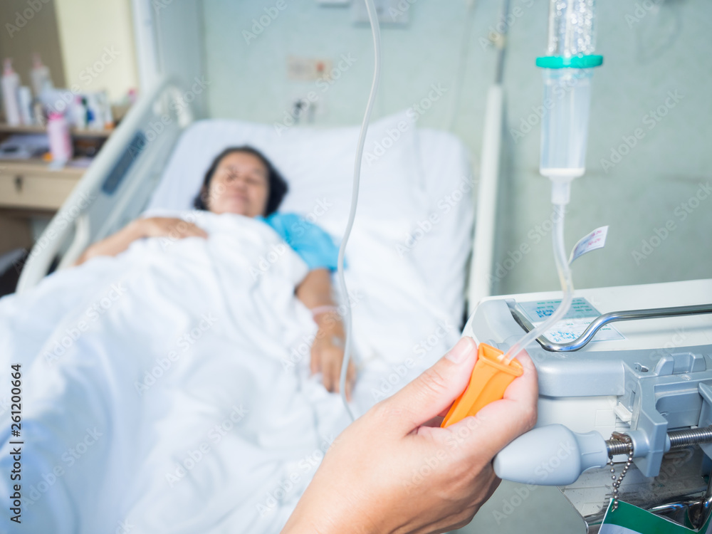 Obraz premium Close up nurse hand adjust set iv fluid intravenous drop saline drip in hospital room with blurry patient woman on hospital bed.Medical treatment emergency patient.Caregiver and hopeful concept