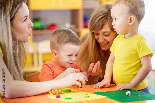 Teacher and cute little kids play with plasticine in preschool