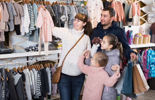 family with daughters showing their purchases in children’s clothes shop