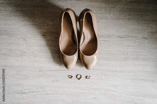Wedding accessory bride. Stylish lacquered beige shoes, earrings, gold rings are isolated on table standing on wooden background. flat lay. top view