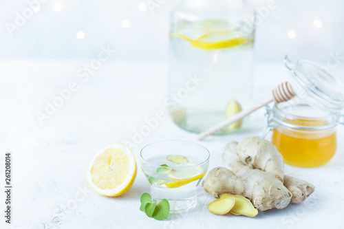 Healthy ginger drink in a cup. Ginger root, honey in a jar, lemon on a white table.